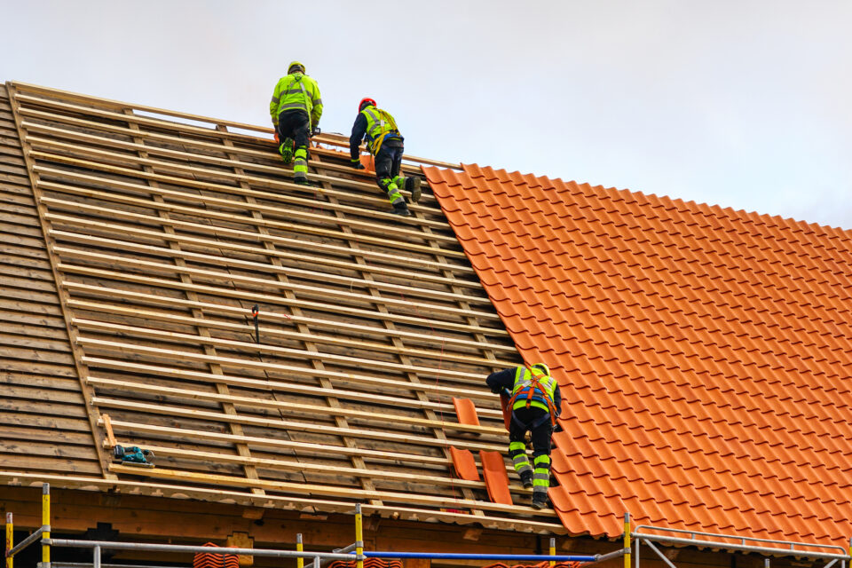 Three roofers in protective workwear installing new clay tiles, new clay tiles layer covering